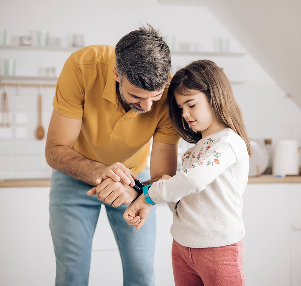 Ein Mann mit einem Kind sind zu sehen, beide stellen gemeinsam ihre Smartwatch ein.