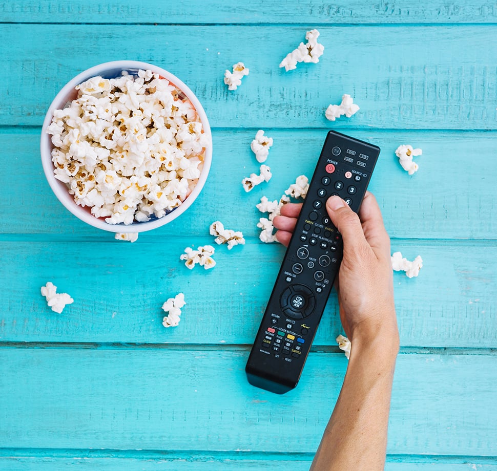 Eine Fernbedienung und eine Schüssel voll Popcorn sind auf einem blauen Tisch.