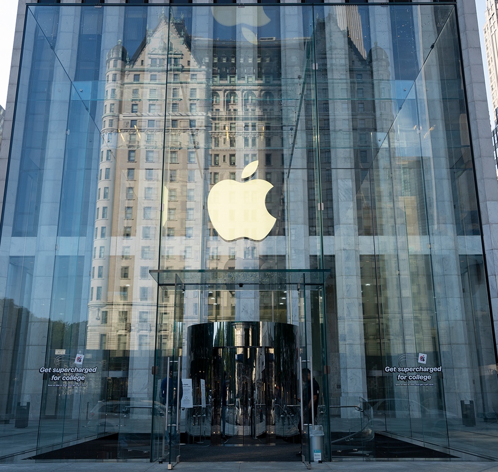 Der Eingang eines Apple Stores ist zu sehen. Im Fenster spiegelt sich ein weiteres Gebäude.