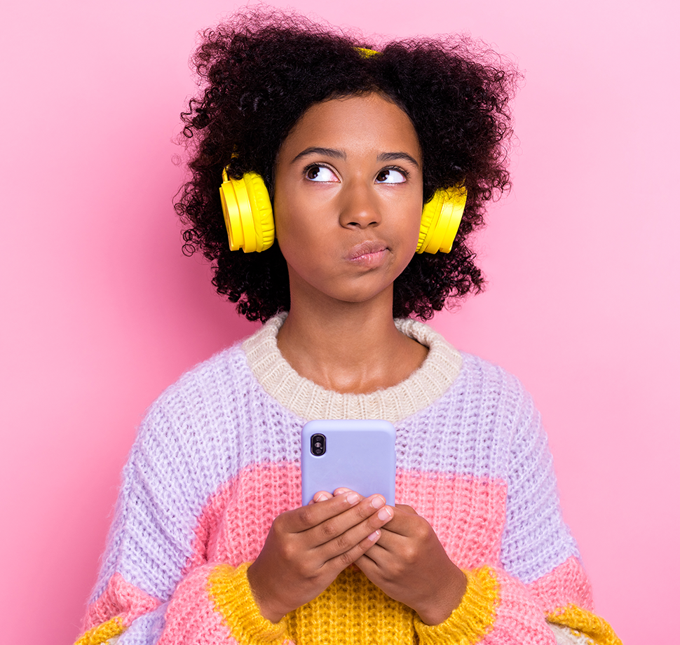 Ein Kind hat gelbe Kopfhörer auf und schaut nachdenklich an die Decke. In ihrer Hand hält das Kind ein Smartphone mit einer violetten Hülle.