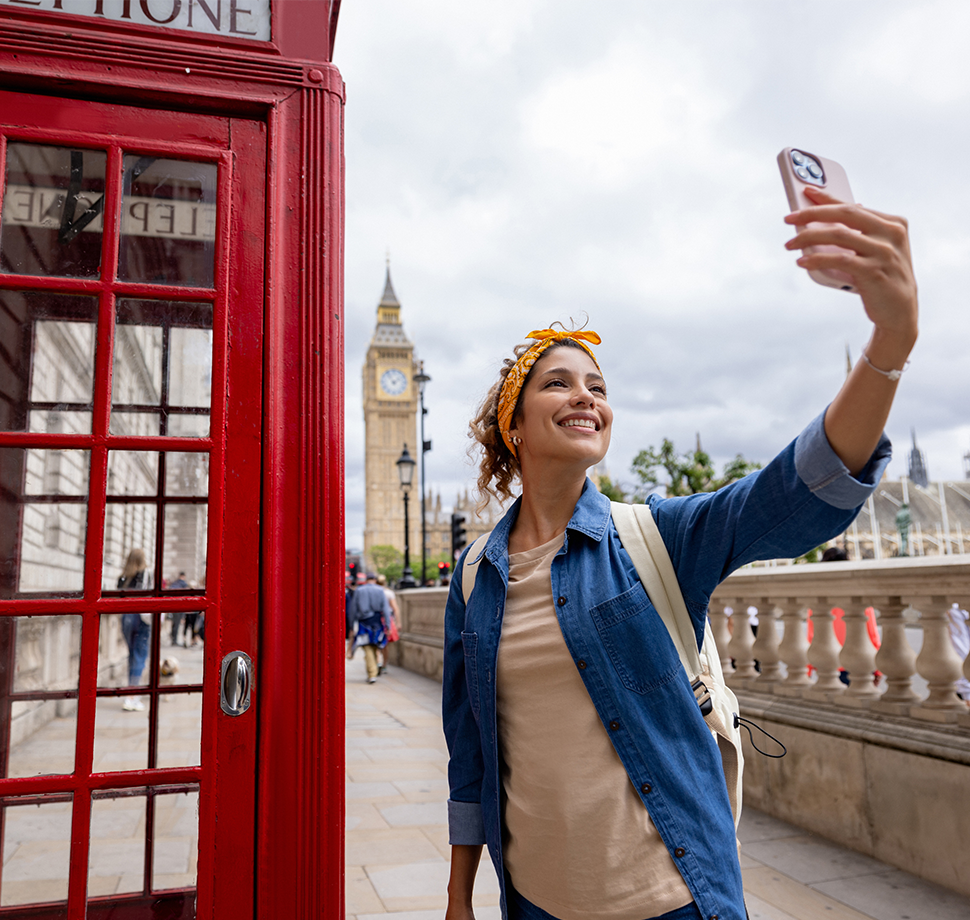 Eine Frau schaut neben einer britischen Telefonzelle auf ihr Handy. Im Hintergrund ist der Big Ben zu sehen.