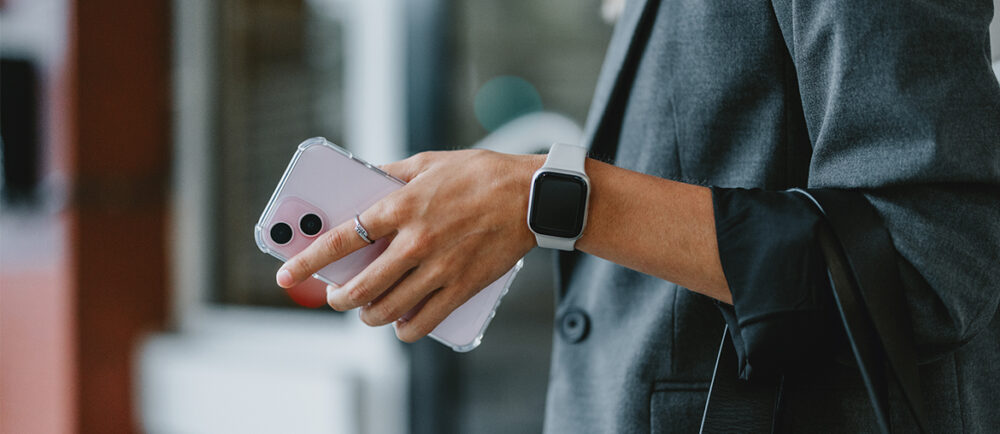 Eine Person hat ein Handy in der Hand und trägt eine Smartwatch. Smartwatch mit Vertrag Blogbeitrag Titelbild