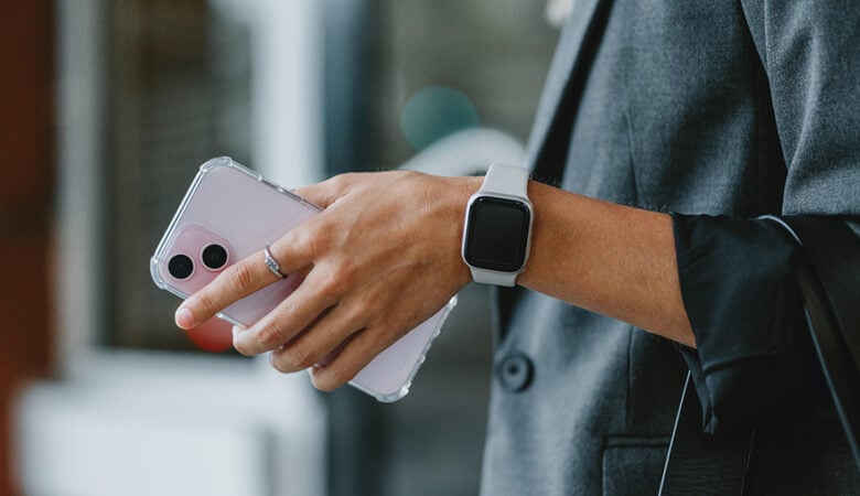 Eine Person hat ein Handy in der Hand und trägt eine Smartwatch. Smartwatch mit Vertrag Blogbeitrag Titelbild